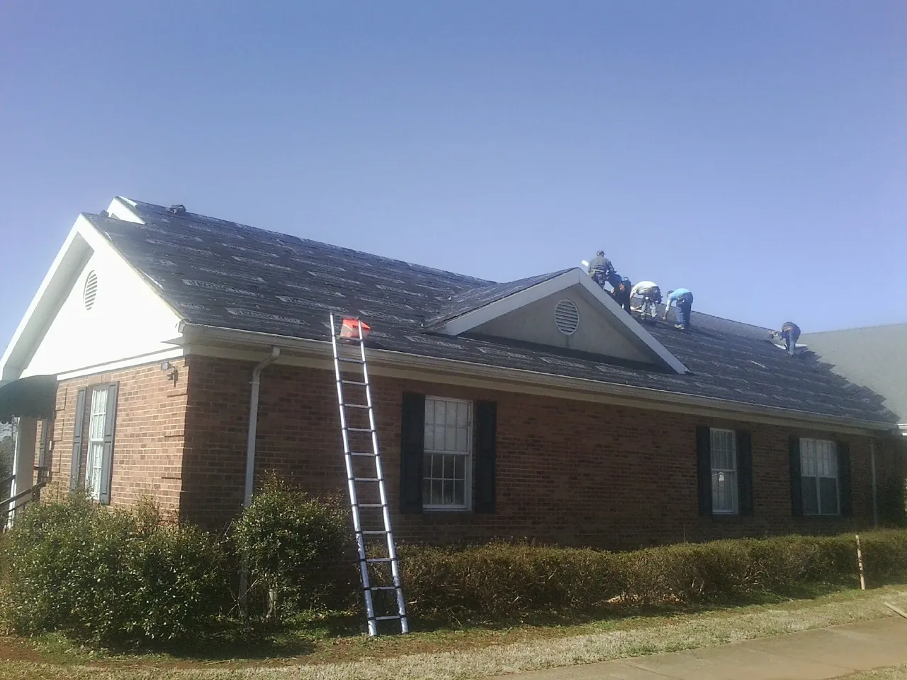 Crew tearing shingles off a brick ranch roof with a ladder set — Metal Roof Repair work by our crew in Isle Of Palms