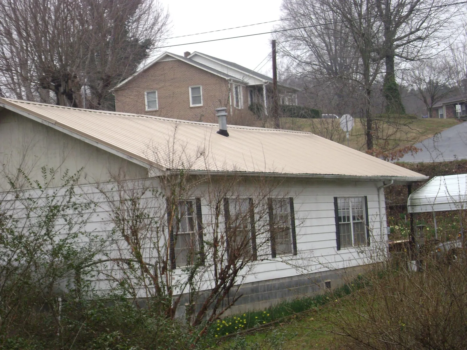 Tan metal roof on a white sided house set into a hillside — Commercial Roofing by Roofing Brothers in Isle Of Palms